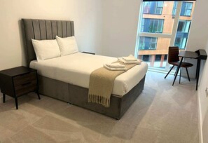 A bedroom with a bed, bedside tables, a chair, and a view of buildings through a window.
