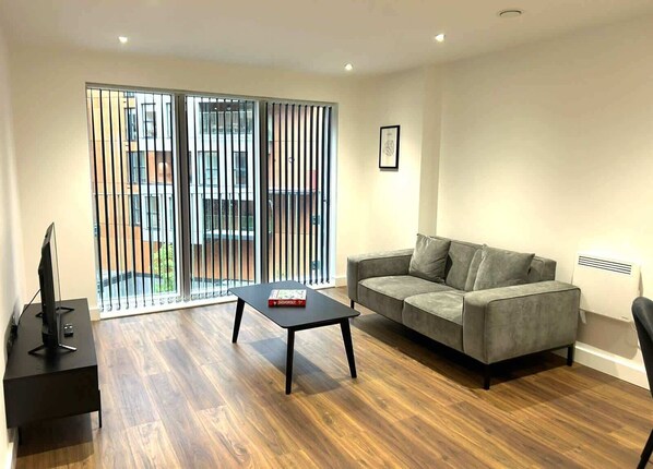 A modern living room with a grey sofa, a black coffee table, and a TV on a black stand.