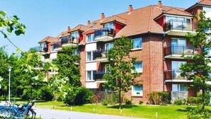 Un immeuble résidentiel à plusieurs étages, avec une façade en briques, des balcons et un espace de stationnement pour vélos.