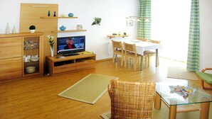Un salon comprenant un téléviseur, une table à manger, des chaises et un fauteuil en osier.