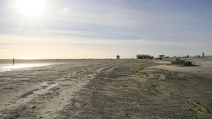 Een breed zandstrand met een heldere lucht en een paar gebouwen in de verte.