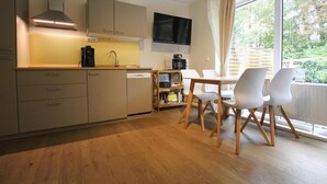Een moderne keuken met een eethoek, houten keukenkastjes, een ingebouwde oven, een koffiezetapparaat en een aan de muur bevestigde televisie.