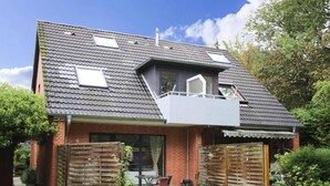 Een tweelaags huis met een schuin dak, een balkon en een omheinde achtertuin.