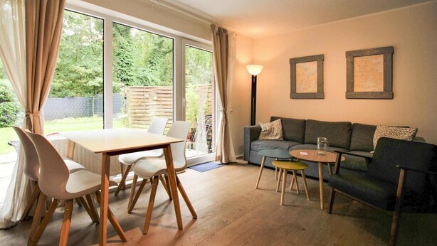 Een woonkamer met houten vloer, een eettafel met stoelen, een bank en een lamp.