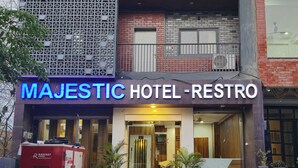 L’extérieur du Majestic Hotel-Restro se distingue par sa façade moderne, son entrée imposante, ses plantes en pot et son unité de climatisation bien visible.