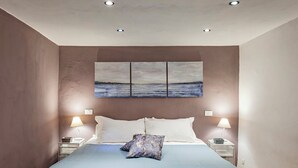Un dormitorio con una cama, dos lámparas de noche, una mesita de noche y un cuadro sobre la cama.