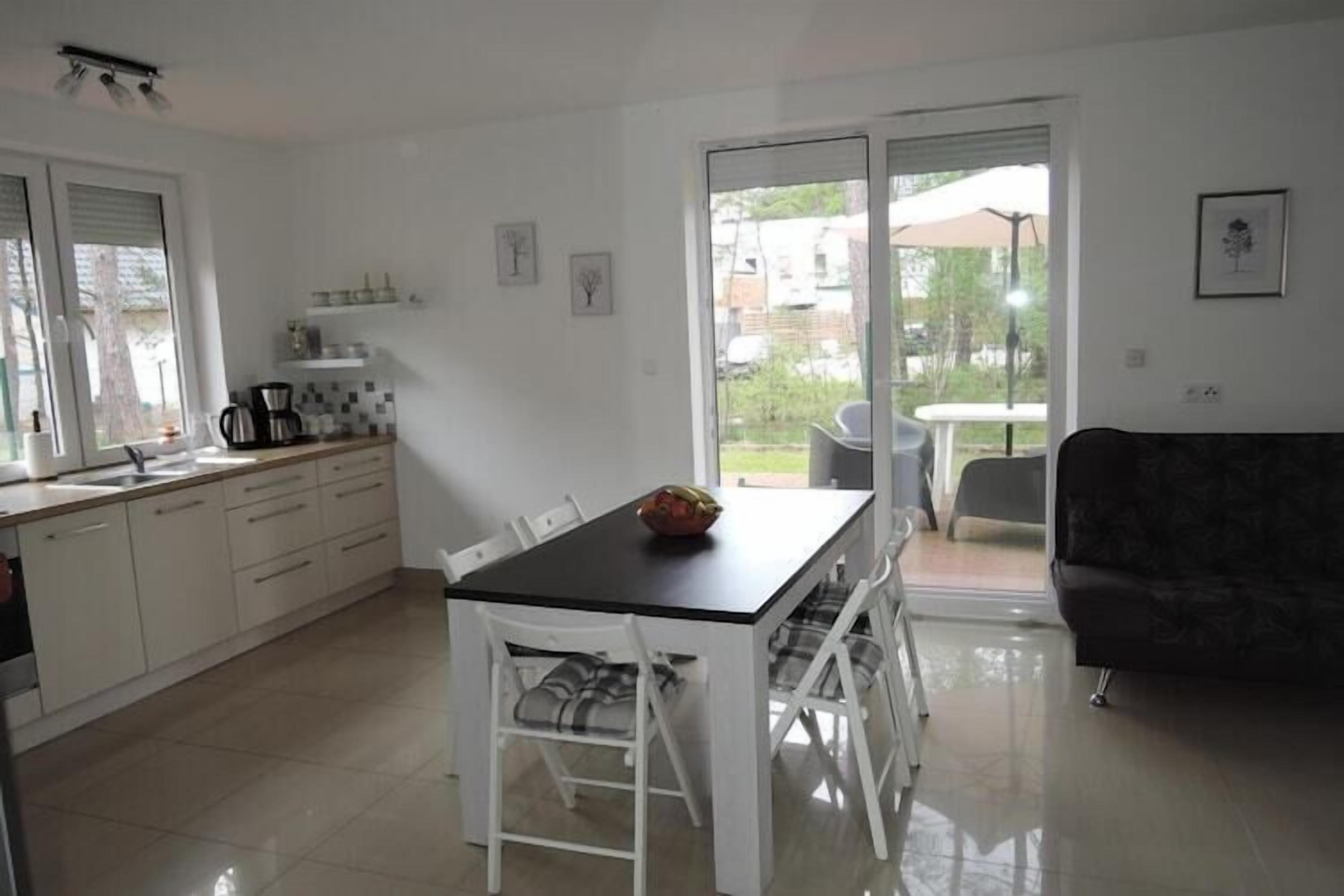 A modern kitchen with white cabinets, a black countertop, and a dining table with chairs. There is a sliding glass door leading to an outdoor area with a table and chairs.