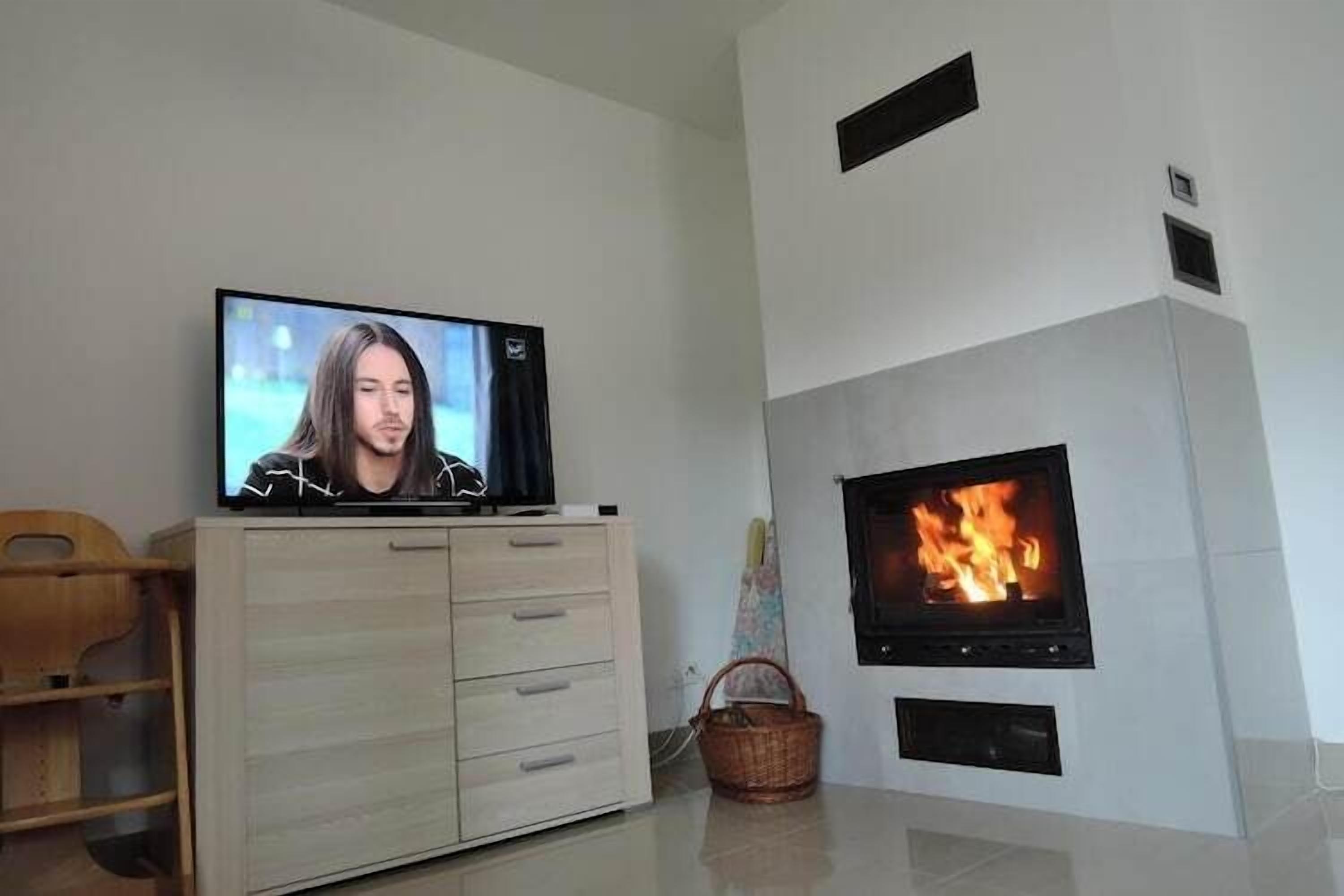 Ein modernes Wohnzimmer mit einem Flachbildfernseher auf einer Holzkommode, einem Kamin mit brennendem Feuer und einem Korbwäschesack auf dem Boden.