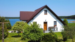 A white house with a brown roof, a wooden door, and a small window. There is a bench and a table outside. - Comfortable holiday apartment with a lake view (Lipnica)