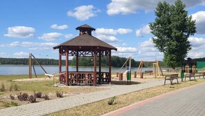 A gazebo with a roof, surrounded by a paved area with benches and swings. - Comfortable holiday apartment with a lake view (Lipnica)
