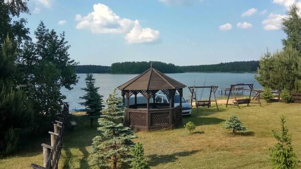 A gazebo with a wooden lattice roof, a swing set, and a car parked nearby. - Comfortable holiday apartment with a lake view (Lipnica)