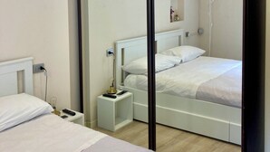 Habitació d'hotel moderna amb un gran mirall, un llit amb roba de llit blanca, una taula de nit amb una làmpada i un aire condicionat fixat a la paret.