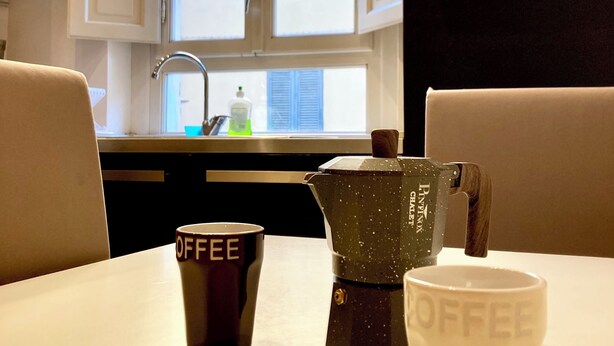 Cuina amb finestra, cafetera i dues tasses de cafè sobre una taula.