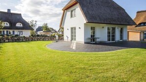 Ein modernes Haus mit steiler Dachneigung, einer Steinmauer und einem gepflegten Rasen.