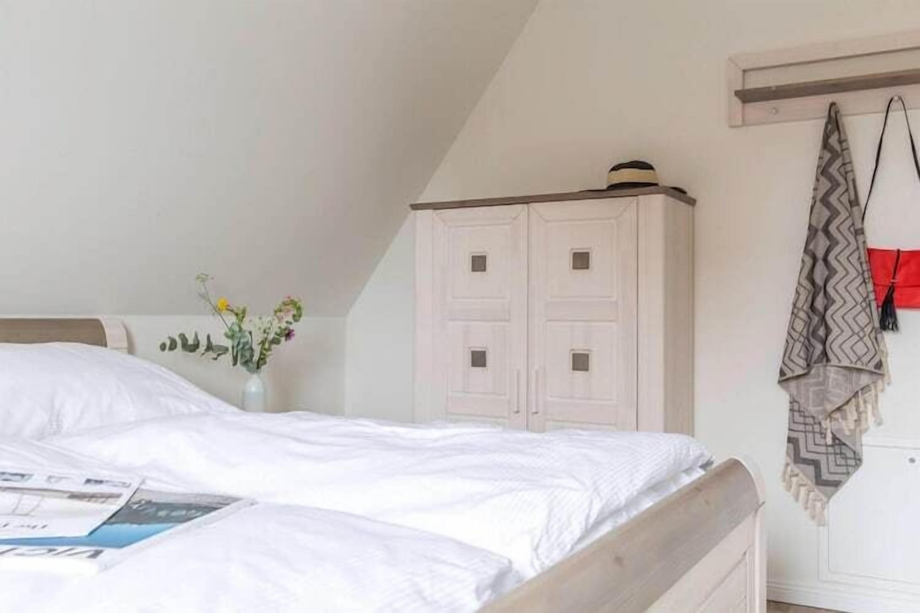Un dormitorio con cama, un armario blanco y una mesita con un jarrón de flores.