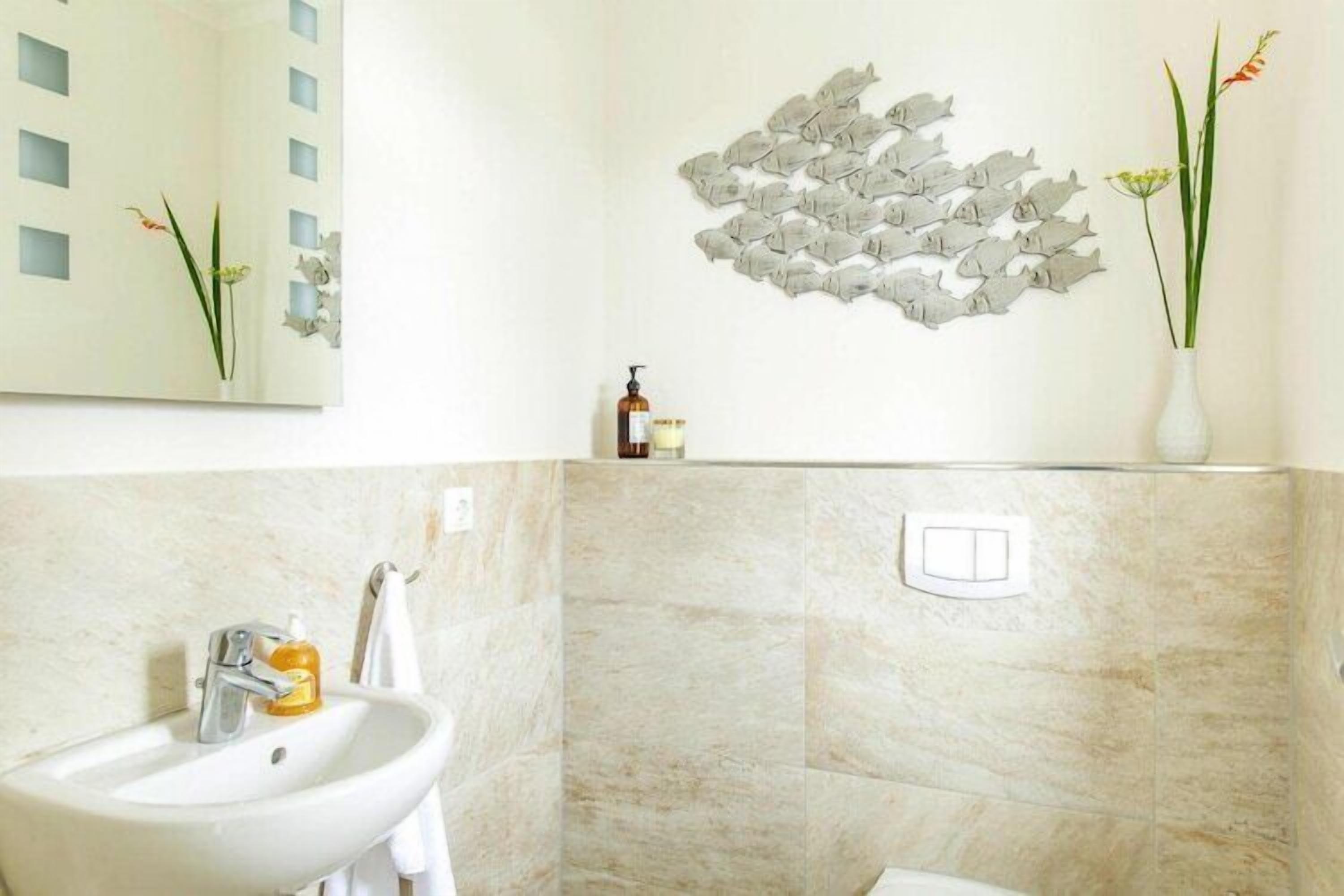 A bathroom with a sink, mirror, and decorative fish wall art.
