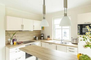 A modern kitchen with white cabinets, a wooden countertop, and pendant lighting.