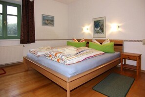 A bedroom with a wooden bed, a green pillow, a bedside table, and a window with curtains.