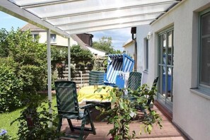 A covered patio area with outdoor furniture, a transparent roof, and surrounding greenery.