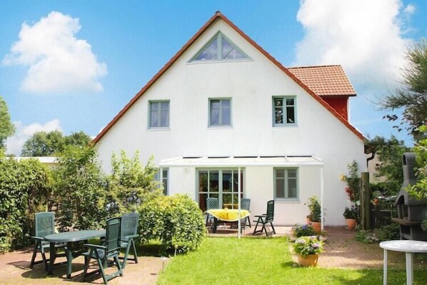 A two-story house with a red-tiled roof, a covered patio, and a small garden with a table and chairs.
