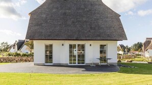 A modern house with a thatched roof, white exterior walls, and large glass doors.