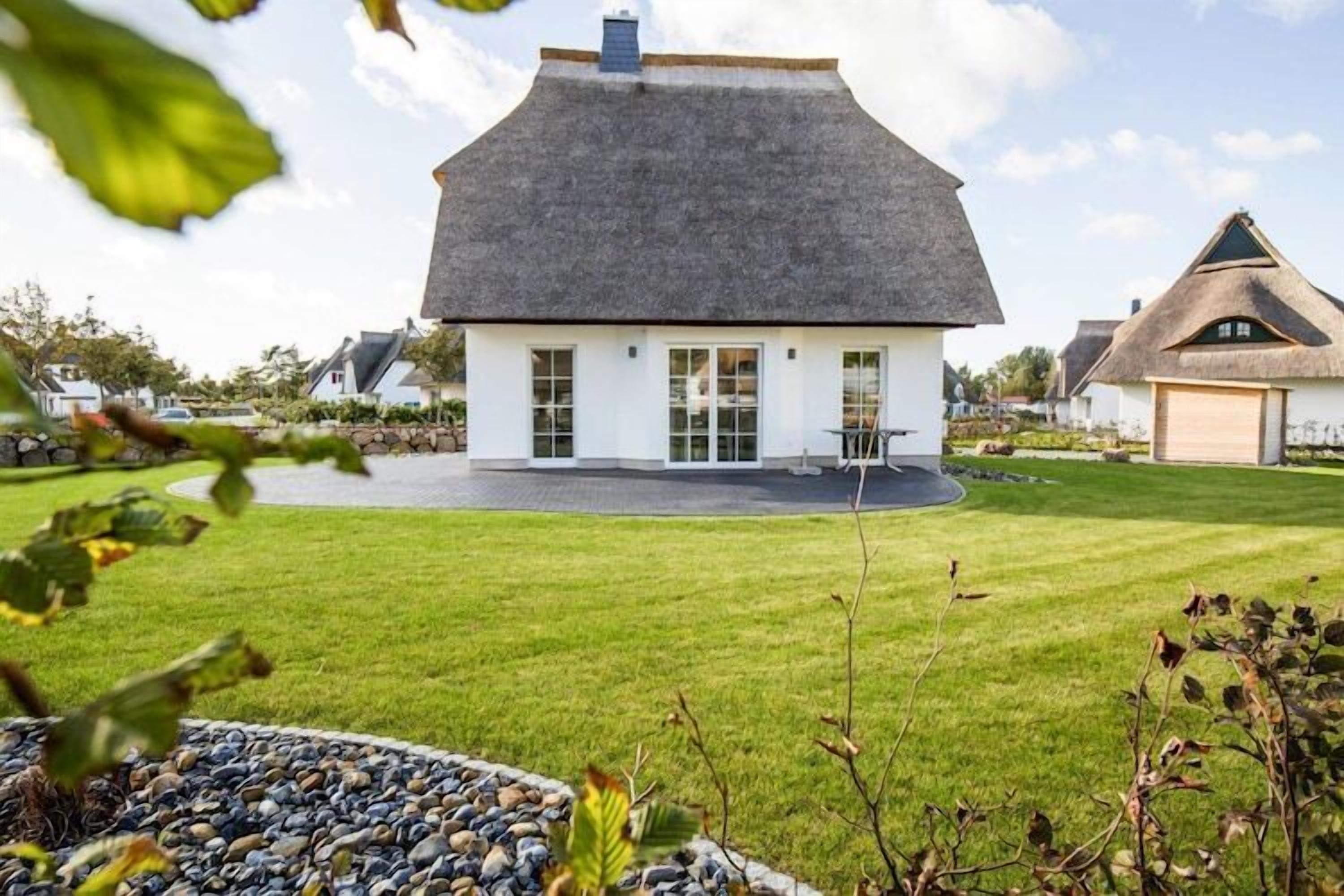 Et hus med hvide vægge og mørkt tag, omgivet af en velplejet græsplæne og en stenskikkelse.