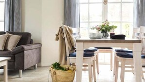 A cozy living room with a sofa, a dining table with chairs, and a window with curtains.
