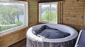 A cozy cabin room with a circular bed, wooden walls, and large windows offering a view of a lake and trees.