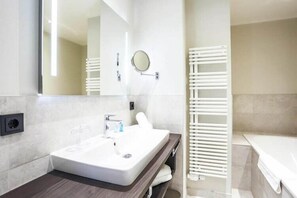 Un baño moderno con un espejo grande, un lavamanos blanco, un perchero y una bañera blanca.