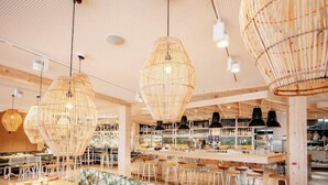 Un interior moderno con lámparas colgantes de mimbre, una zona de bar con taburetes y un área de estar con cojines estampados.