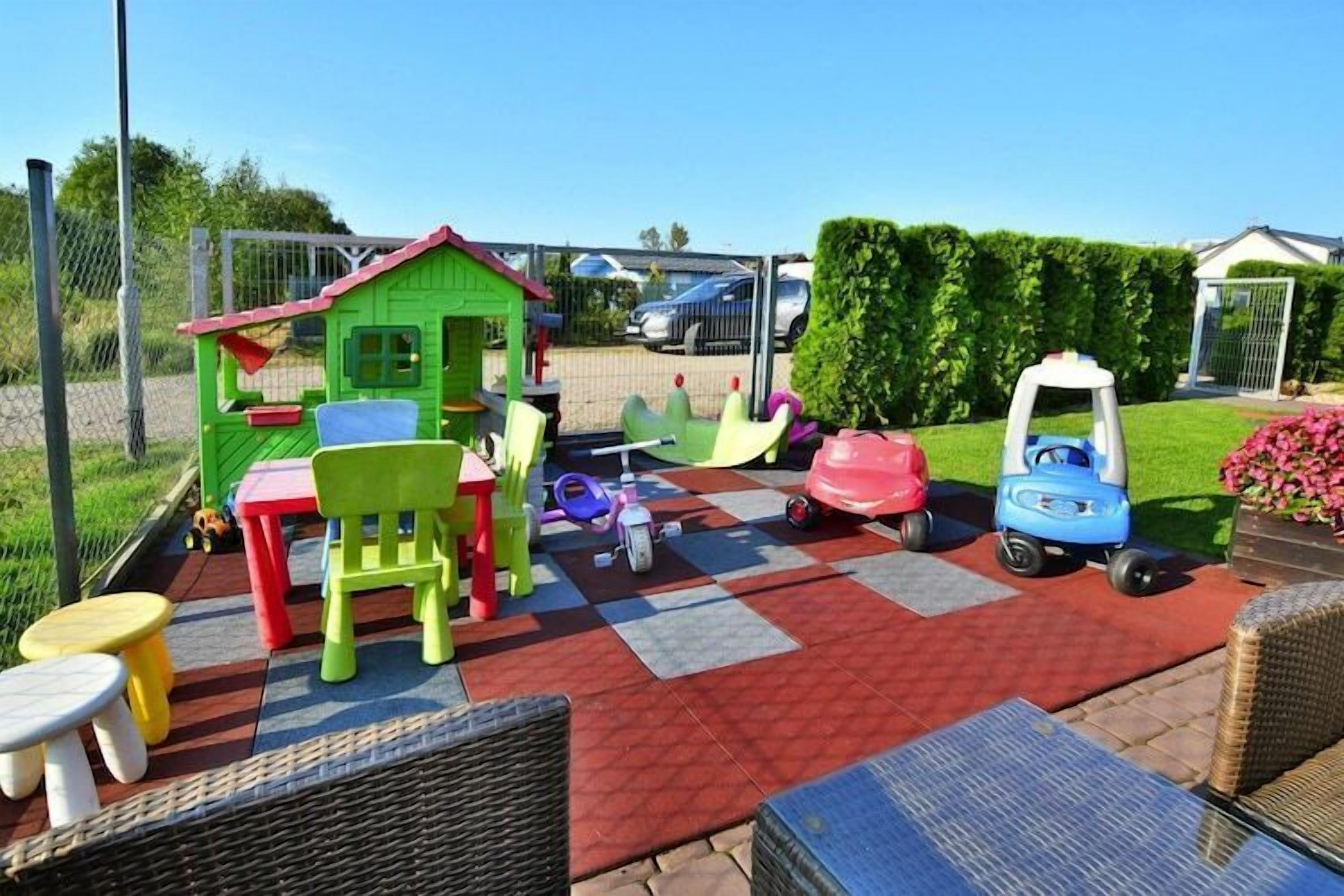 Un área de juegos infantiles con una casita, sillas coloridas, mesas y un coche de juguete.