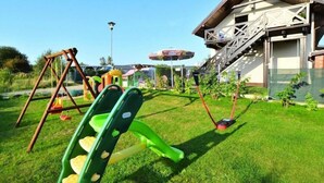 A grassy outdoor area with a swing set, a slide, and a climbing structure.