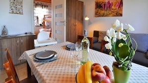 A dining area with a table set for two, a bowl of fruit, a bottle of olive oil, and a potted plant.