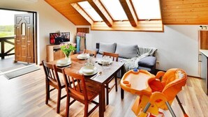 A dining area with a wooden table and chairs, a sofa, and a child’s high chair.