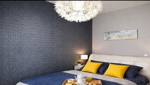 A modern bedroom with a patterned wall, a bed with blue and yellow bedding, a bedside table with a lamp, and a tray with breakfast items. - Apartment in Rewal near Blue Flag Beach (Rewal)