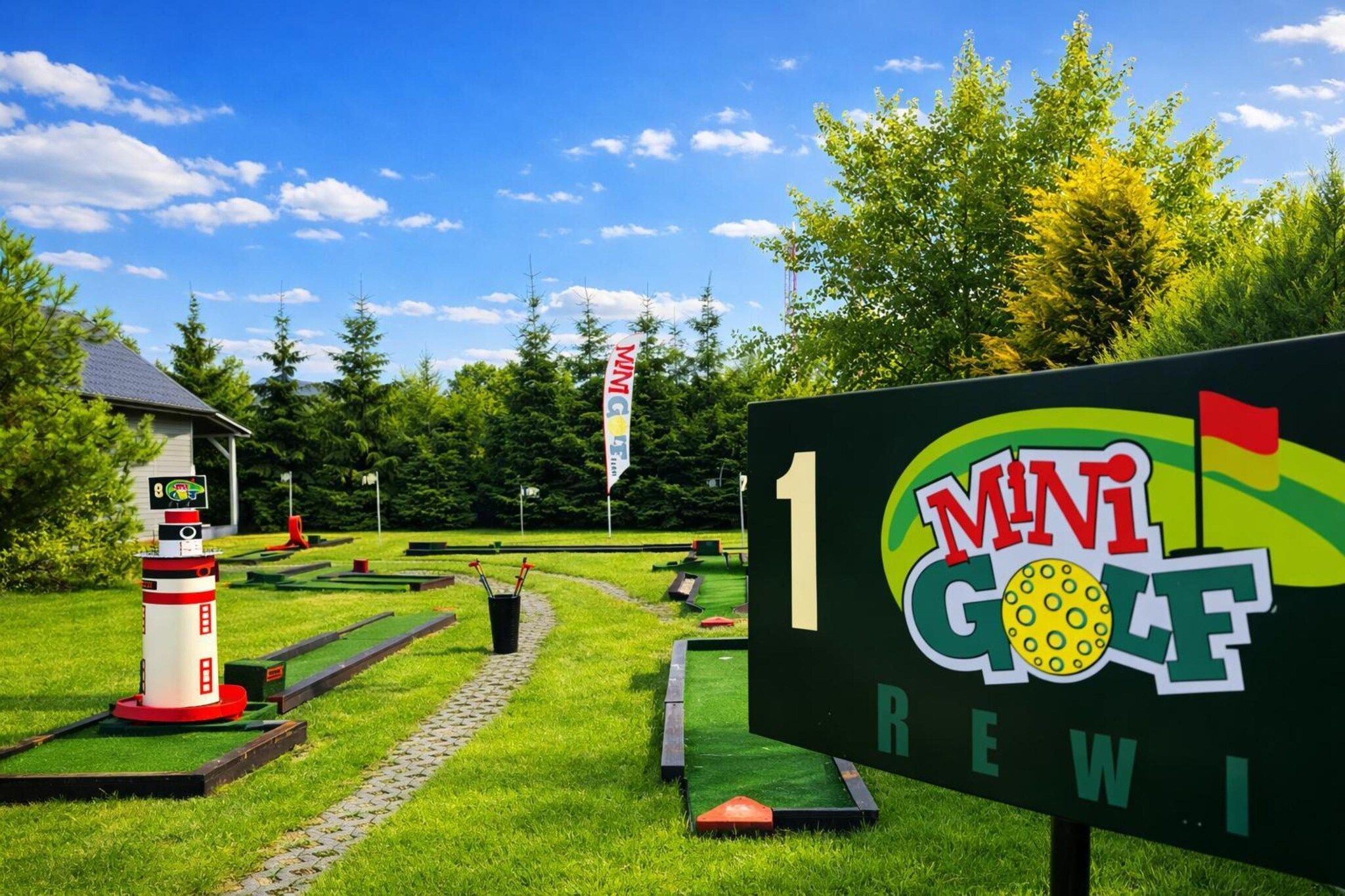 Un parcours de mini-golf avec une enseigne indiquant « Mini Golf Rewi » et une maquette de phare.