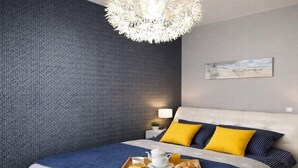 Une chambre moderne avec un mur à motifs, un lit avec une literie bleue et jaune, une table de chevet avec une lampe et un plateau contenant des éléments pour le petit-déjeuner.