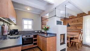 A compact kitchen with wooden cabinets, a built-in oven, a sink, and a dining area with a wooden table and chairs. - Ferienhäuser, Torfhaus (Torfhaus)