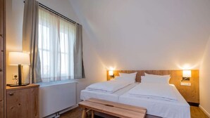 A bedroom with a bed, bedside lamps, a bench, and a window with curtains. - Ferienhäuser, Torfhaus (Torfhaus)
