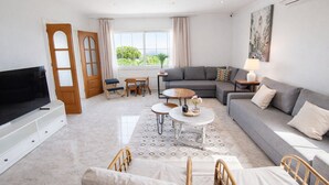 En moderne stue med et fladskærms-tv, en sofa, et sofabord og et spiseområde med stole og bord.