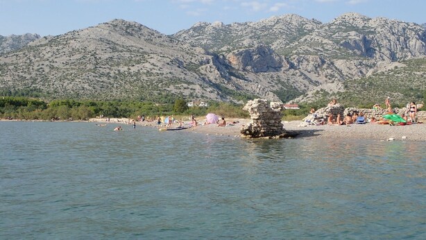 Une plage où l’on voit des gens nager et se détendre, un promontoire rocheux et, au loin, des montagnes.