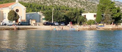 A coastal area with a church, parked cars, and people near the water.