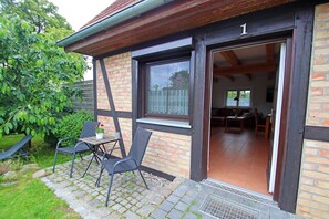 A brick building with a number '1' sign, a patio with chairs and a table, and a covered outdoor area. - Ferienhof Neuendorf (Lütow)