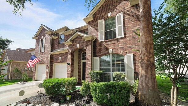 A two-story brick house with a garage, a front porch, and a well-maintained lawn.