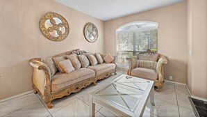 A room with two ornate sofas, a glass coffee table, and decorative mirrors on the walls.
