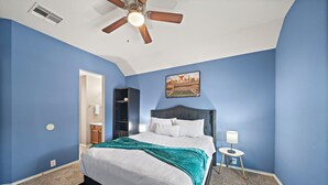 A bedroom with a bed, a ceiling fan, a nightstand, and a wall-mounted TV.