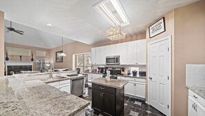 A modern kitchen with white cabinets, a granite countertop, a microwave, and a chandelier.