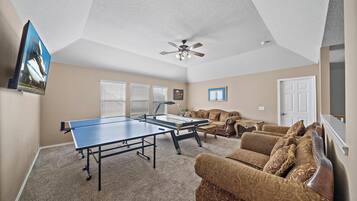 A living room with a ping pong table, a ceiling fan, and a sofa.