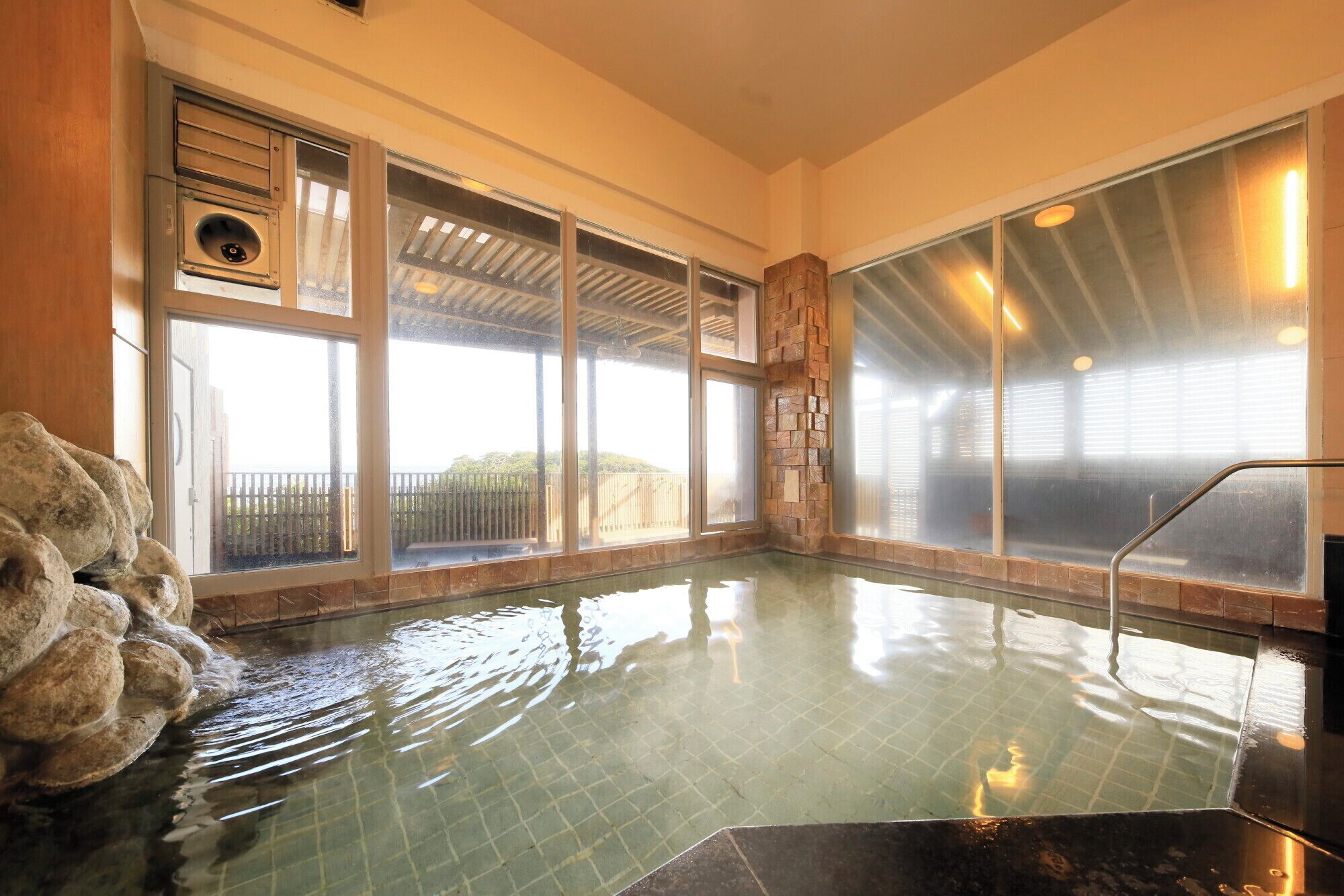 A hot tub with a stone wall and large windows.