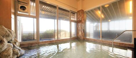 A hot tub with a stone wall and large windows.